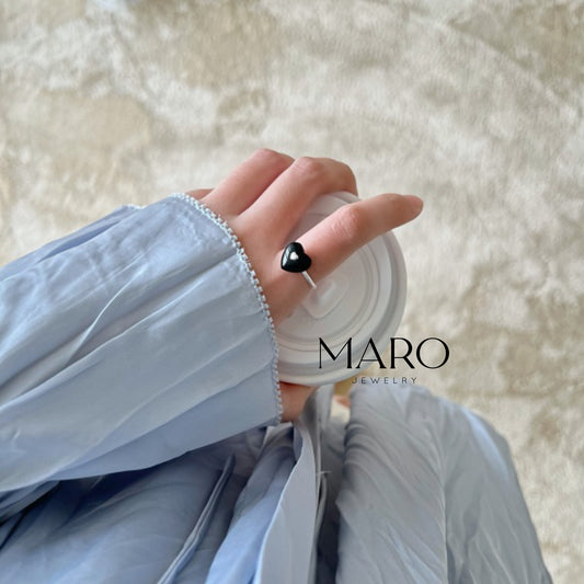 Mano con un anillo de corazón negro, con una manga azul claro y un fondo suave