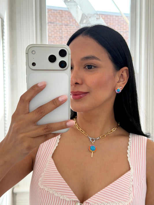 Woman taking a mirror selfie in a striped top, wearing a gold-tone chain necklace with a blue charm