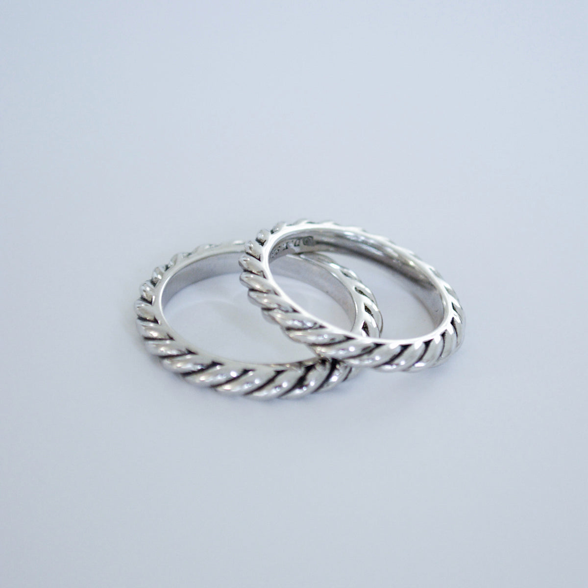 Two slim twisted rope-style silver-tone rings side by side on a pale blue background