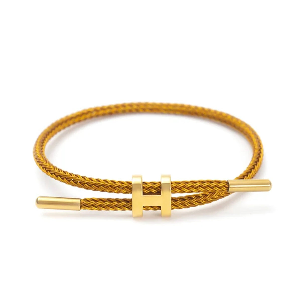 A product photo of a minimalist gold bracelet. The bracelet features a braided gold-colored cord and a sleek, adjustable gold metal clasp in the shape of a capital "H." The background is a clean white.