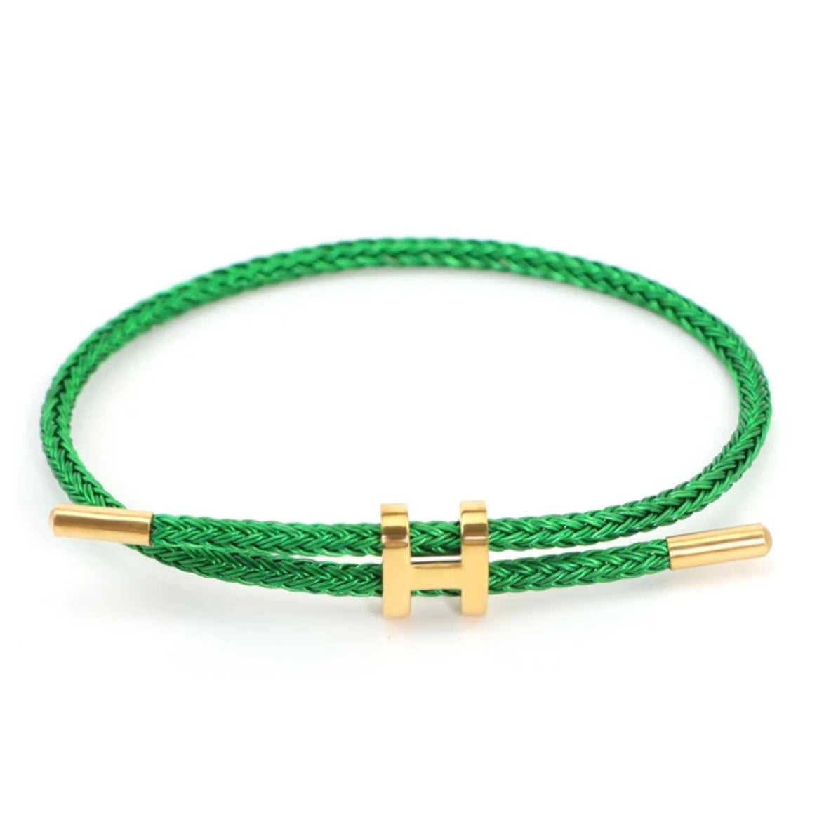 A high-resolution product shot of a minimalist bracelet. The bracelet is made from a vibrant green braided rope and features a shiny gold-colored metal clasp in the shape of a capital 'H'. The clasp is designed to slide, allowing the bracelet to be adjusted. The background is a clean, solid white.