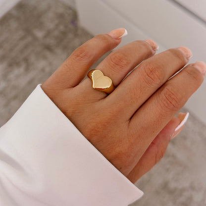 Polished gold heart-shaped ring worn on the ring finger of a female hand with a French manicure, highlighting personal and elegant style.