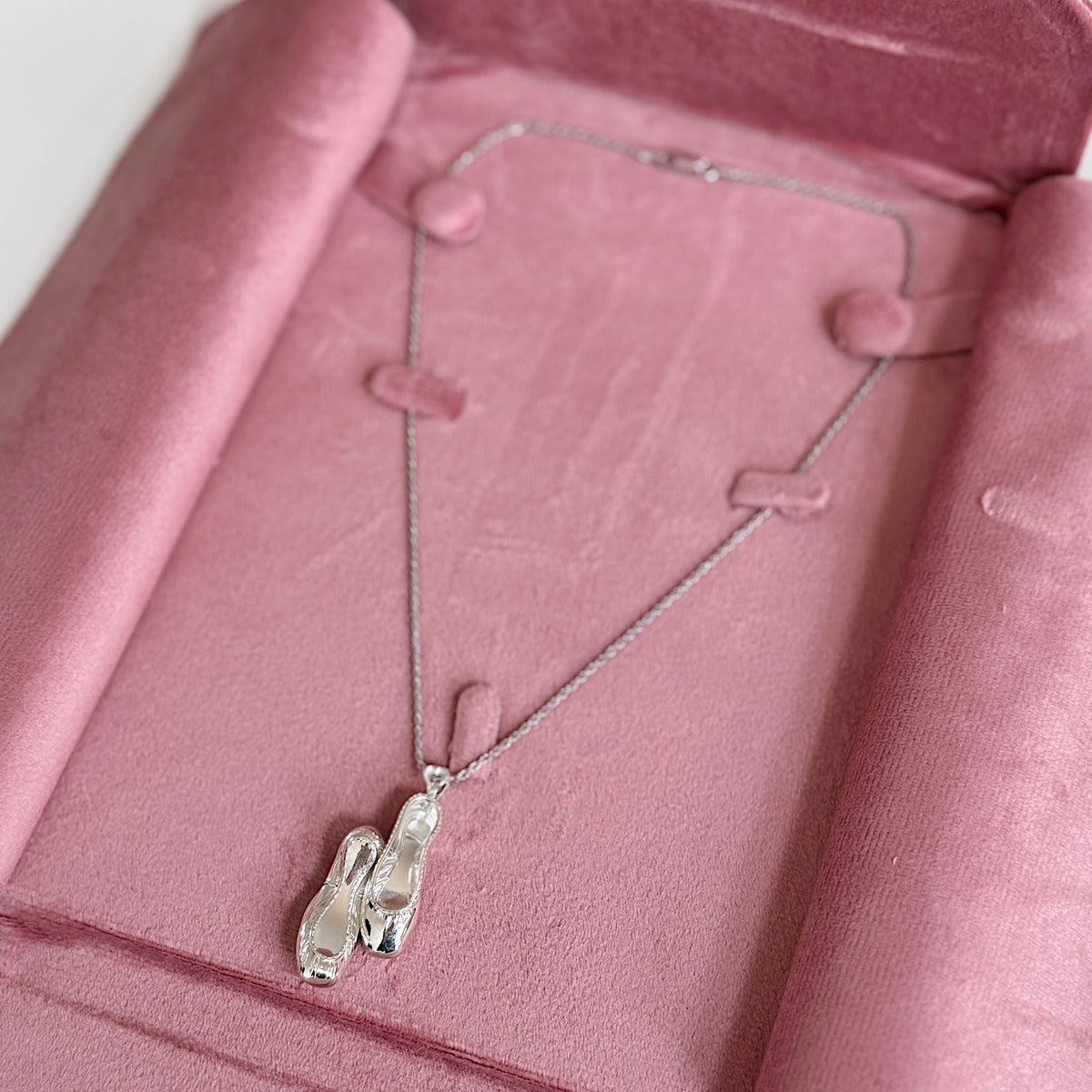 Ballet flats charm on a thin silver-tone chain resting on pink velvet in a jewelry box