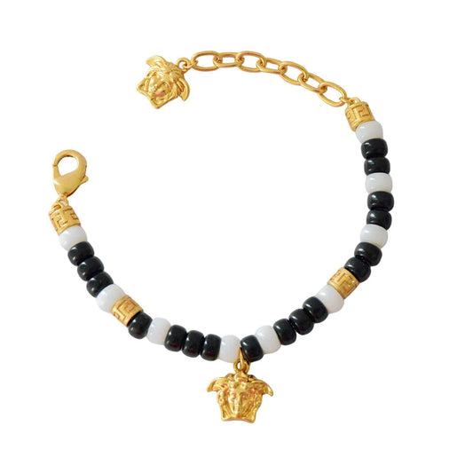 Pulsera de cuentas negras y blancas con separadores de tono dorado, un dije esculpido y cierre de langosta