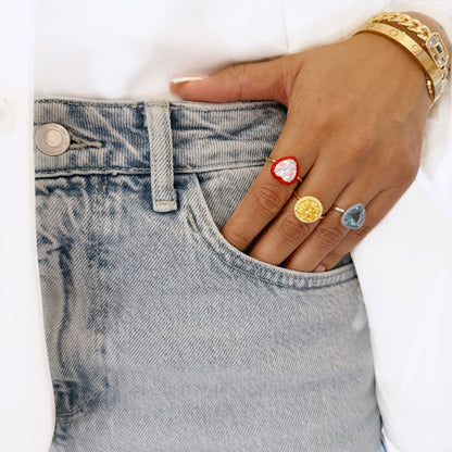 Mano con jeans que lleva anillos de colores con piedras en forma de corazón