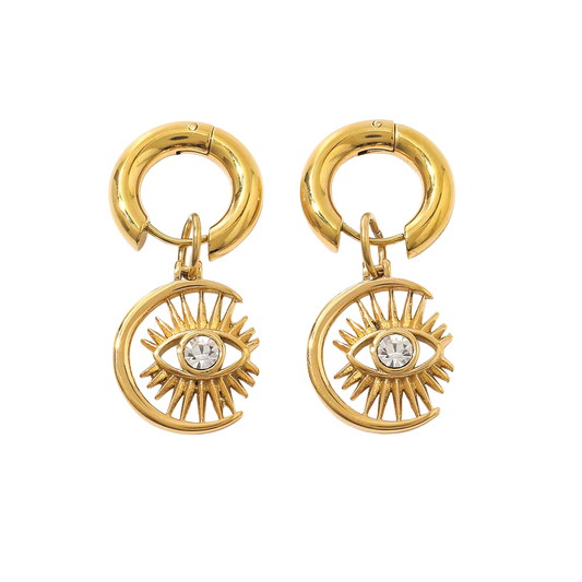 Pair of chunky gold-colored huggie hoops with crescent eye charms on a black background