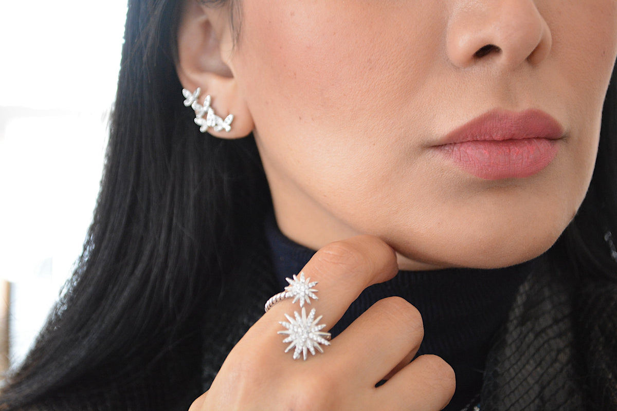 Primer plano del arete de mariposa en la oreja, con un anillo en forma de estrella en su mano