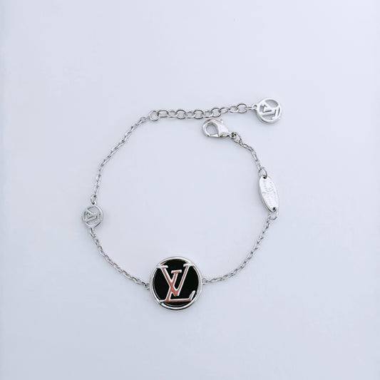 Pulsera de cadena fina de tono plateado con un disco negro redondo y pequeñas placas ovaladas