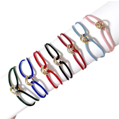 Muchas pulseras de cordón en diferentes colores con tres pequeños anillos entrelazados, exhibidas sobre un soporte blanco