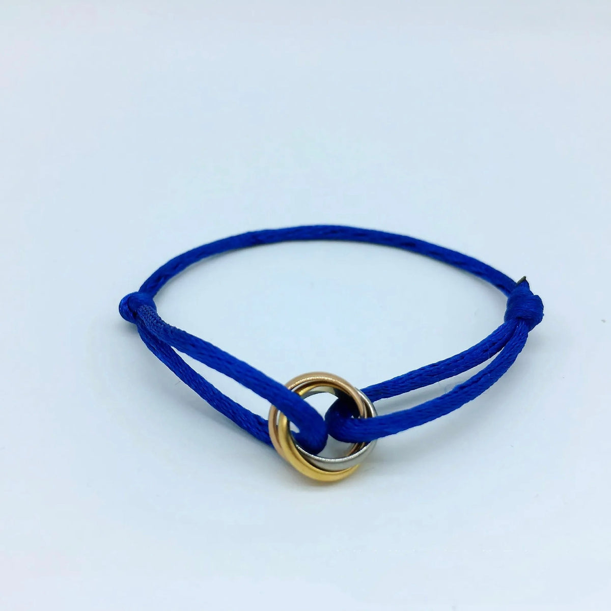 Pulsera de cordón azul rey con tres pequeños anillos entrelazados, sobre un fondo azul claro