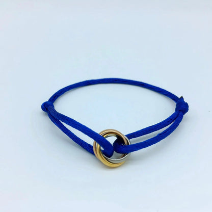 Pulsera de cordón azul rey con tres pequeños anillos entrelazados, sobre un fondo azul claro