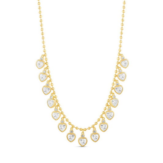 Collar de cadena de bolitas de tono dorado con una hilera de piedras transparentes en forma de corazón, sobre fondo blanco