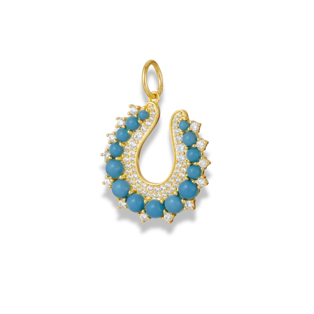 Dije de herradura de tono dorado con cuentas redondas azul aguamarina y piedras transparentes brillantes, con una argolla superior, sobre fondo blanco