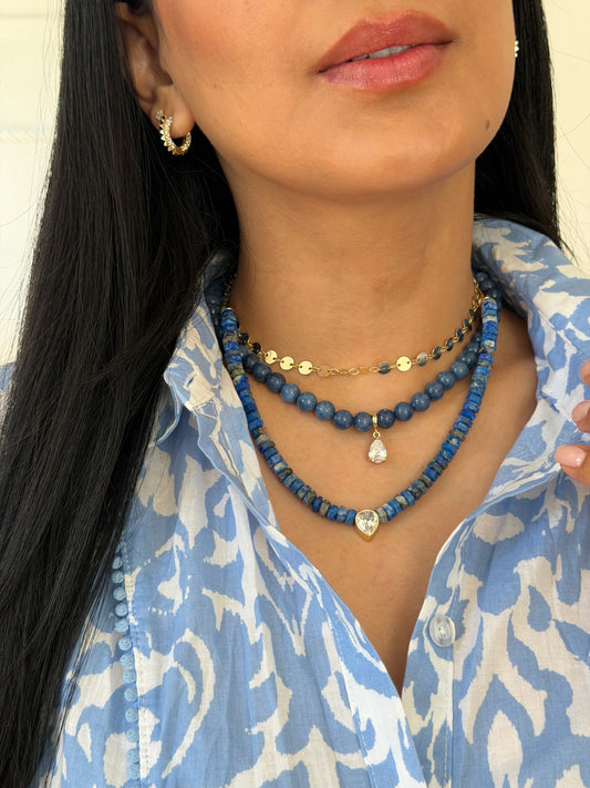 Woman wearing layered blue beaded necklaces with a small gold-tone detail at the neck