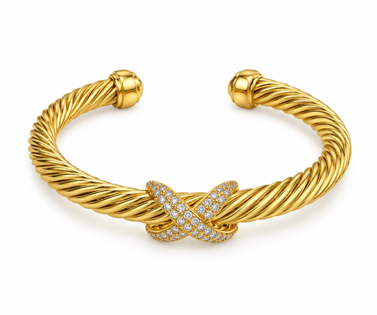 Brazalete abierto trenzado en tono dorado con extremos abombados y una pieza central en forma de X de piedras brillantes diminutas