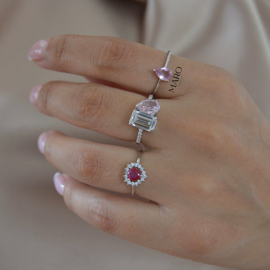 Hand wearing three rings, one with a pink pear-shaped stone and a ring with a clear square stone
