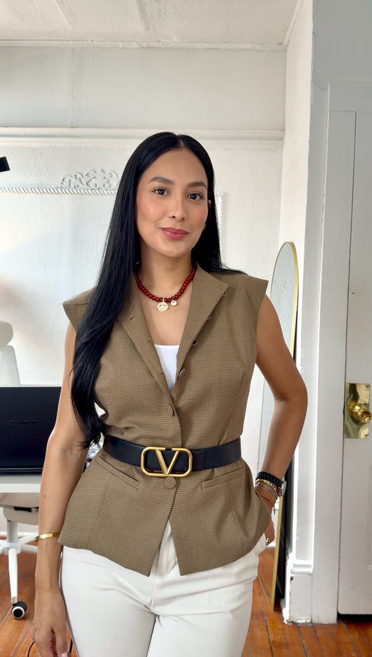 Woman standing in an olive vest and white pants wearing a red bead necklace