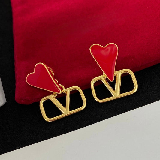 Pair of drop earrings with a red heart above an open gold-tone V-shaped frame, on a red and black backdrop