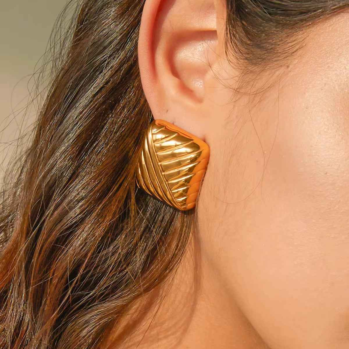 Close-up of a ridged square gold-tone stud earring worn on the ear