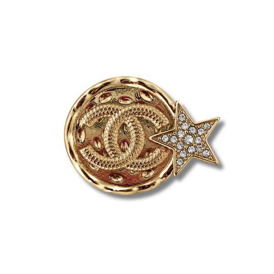 Broche redondo en tono dorado con textura acolchada y una pequeña estrella con piedras transparentes