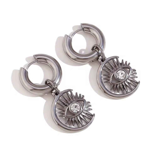 Two silver-color huggie earrings with eye charms hanging from a hinged top, seen at an angle