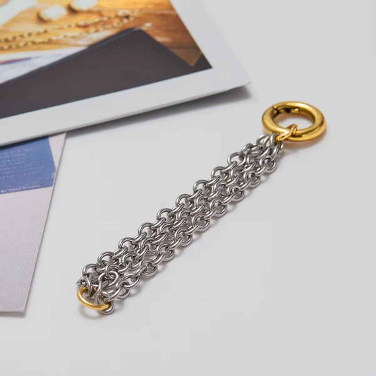 Silver-colored chain links with a round gold-colored clasp, laid on paper in a gray setting