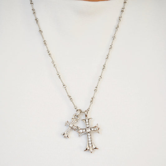 Silver-tone chain necklace with two cross pendants set with clear stones, hanging against a light top