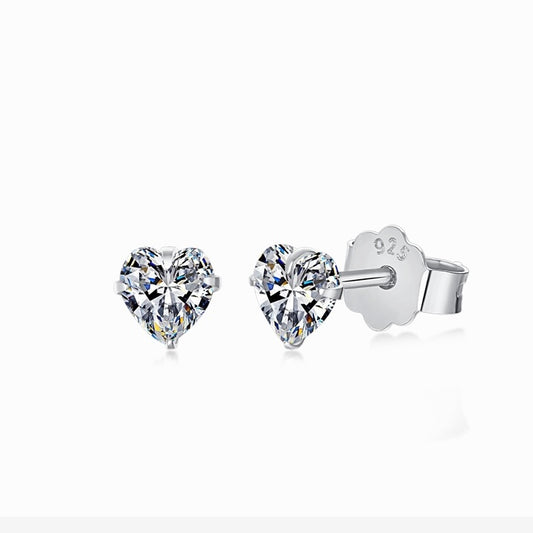 Par de aretes de botón con piedra transparente en forma de corazón y montura en tono plateado, con cierre de poste, sobre fondo blanco