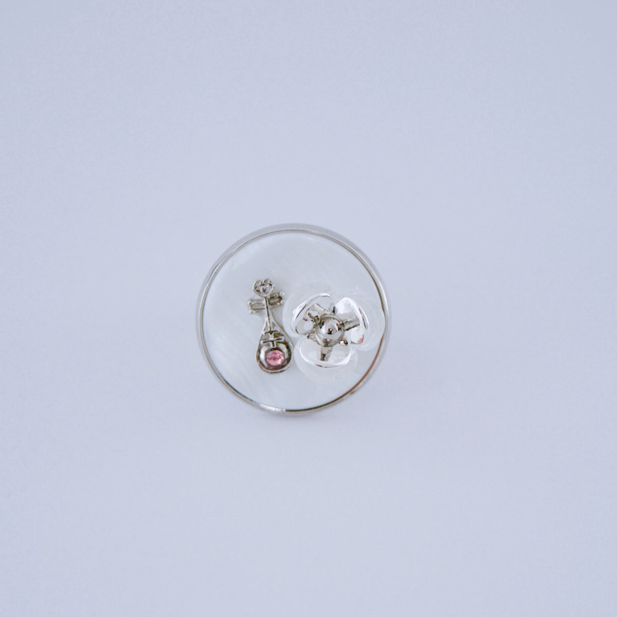 Silver-tone ring with a small stone and flower detail inside a clear round display dome