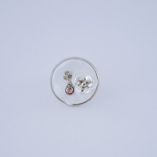 Anillo en tono plateado con una piedra pequeña y un detalle de flor dentro de una cúpula redonda transparente