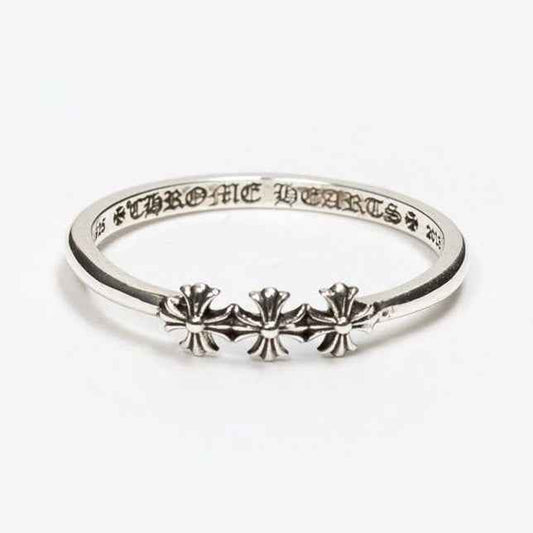 Anillo de banda delgada tono plateado con tres pequeños motivos de flor en forma de cruz y letras grabadas en el interior