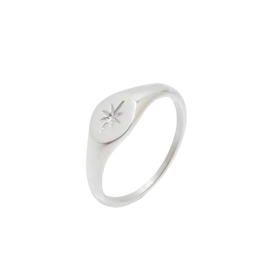 Anillo estilo sello de tono plateado con la parte superior ovalada grabada con una estrella, sobre un fondo blanco