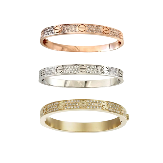 Tres brazaletes cubiertos de piedras apilados en acabados rosa, tono plateado y tono dorado, sobre un fondo blanco
