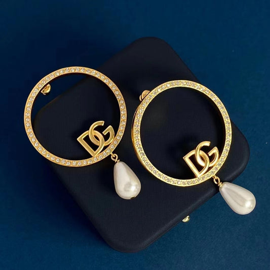 Pair of thin gold-color hoops with clear stones and white teardrop beads on a dark blue box