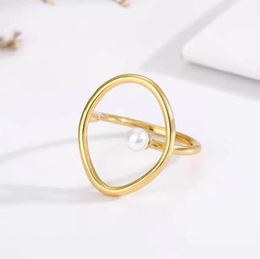 Anillo delgado color dorado con contorno ovalado abierto y una pequeña cuenta de aspecto perlado