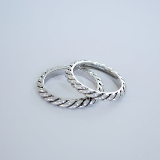 Two slim twisted rope-style silver-tone rings side by side on a pale blue background