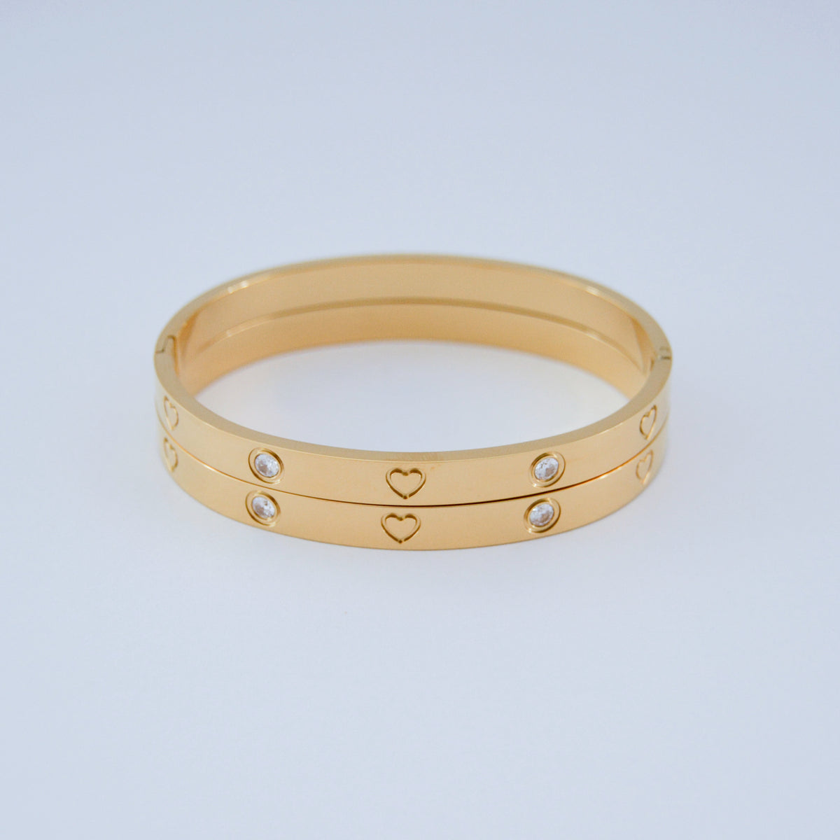 Dos brazaletes de tono dorado con piedras transparentes y corazones
