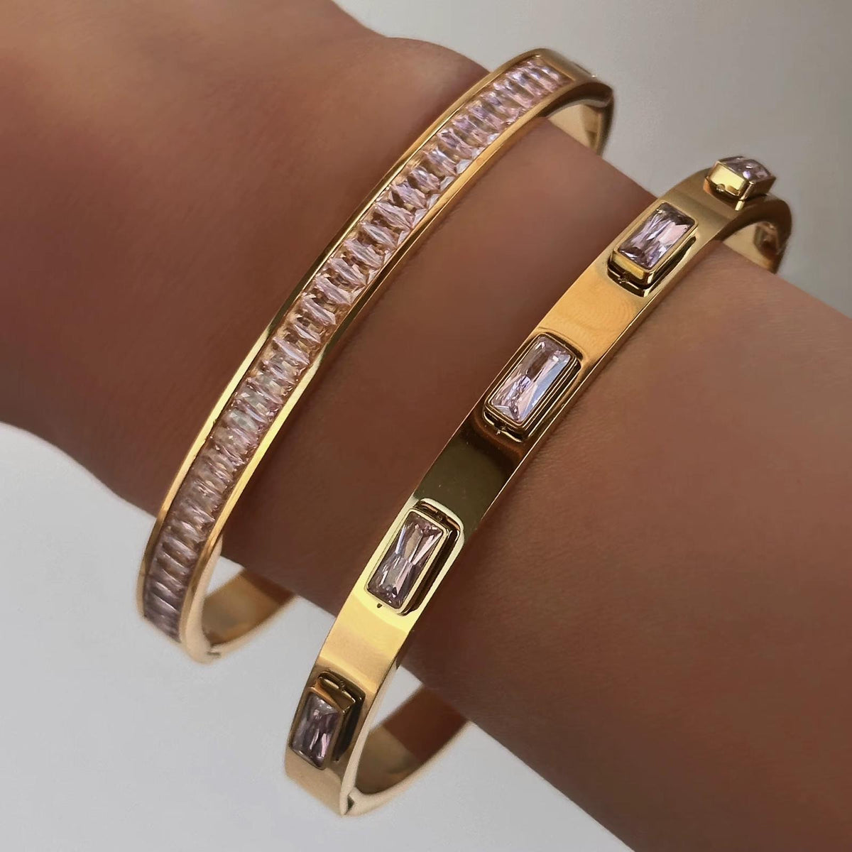 Muñeca con dos brazaletes en tono dorado con piedras rosadas rectangulares