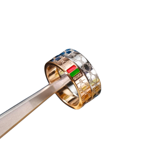 Anillo ancho en relieve de tono dorado con una franja verde y roja sostenido con pinzas