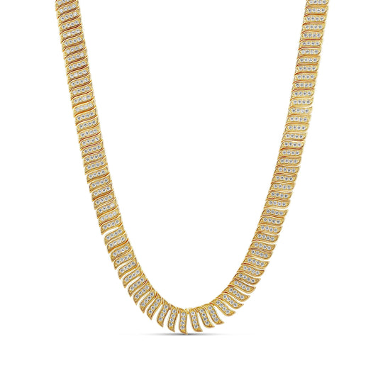 Wide gold-tone necklace of wave-shaped links covered in tiny white stones, laid flat on white