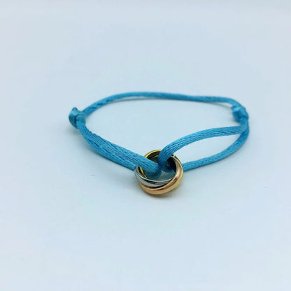 Adjustable pink cord bracelet featuring a tricolor gold and silver interlocking ring charm. Perfect friendship or stacking accessory.